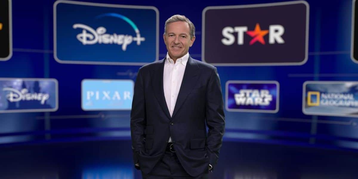 Bob Iger posando em frente a várias telas exibindo várias propriedades de propriedade da Disney