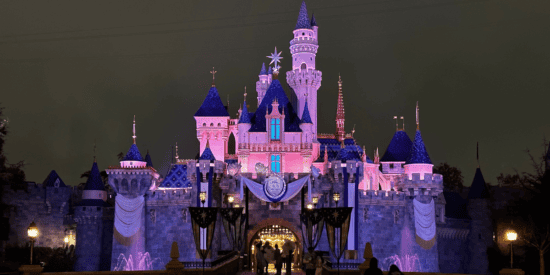 Castelo da Bela Adormecida à noite após a chuva com luzes rosa e as decorações Disney100 no Disneyland Park no Disneyland Resort