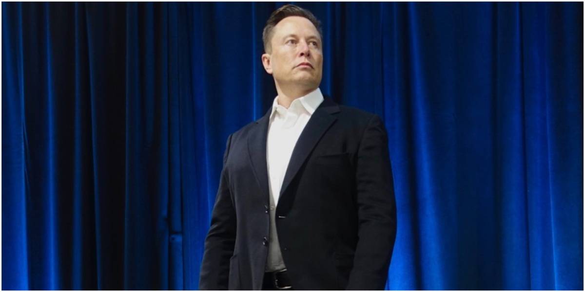 Elon Musk de terno em frente a uma cortina azul